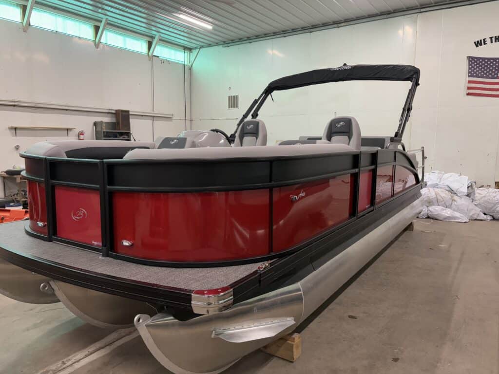 Inside the garage sits a striking 2025 Barletta Aria pontoon boat, featuring a red and silver exterior with sleek black accents, reminiscent of the elegant 22UC model.