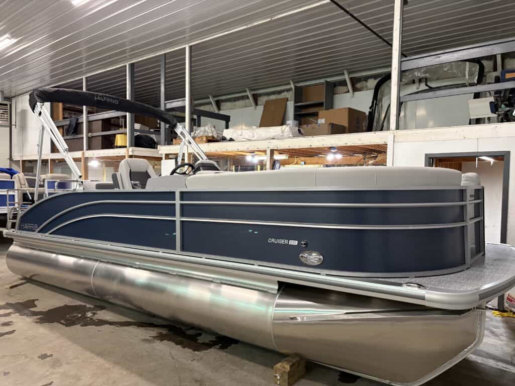 The sleek Harris Cruiser 230 pontoon boat boasts a stylish blue and gray exterior. Safely parked indoors, it features a protective canopy and proudly bears the "Cruiser 190" label, offering a hint of the 2025 yacht experience with its modern design.