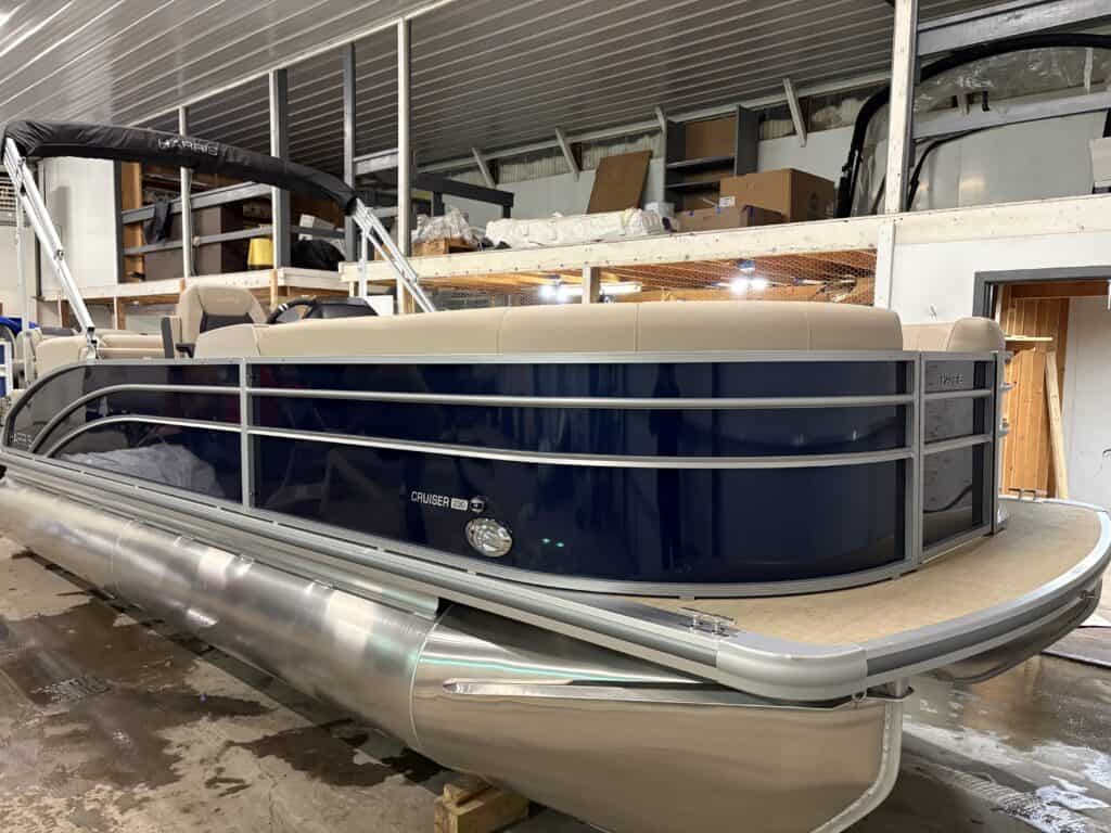 The 2025 Cruiser impresses indoors with its silver pontoons, sleek metal railings, and blue and beige accents. This Harris Cruiser 230 model combines style and comfort effortlessly.